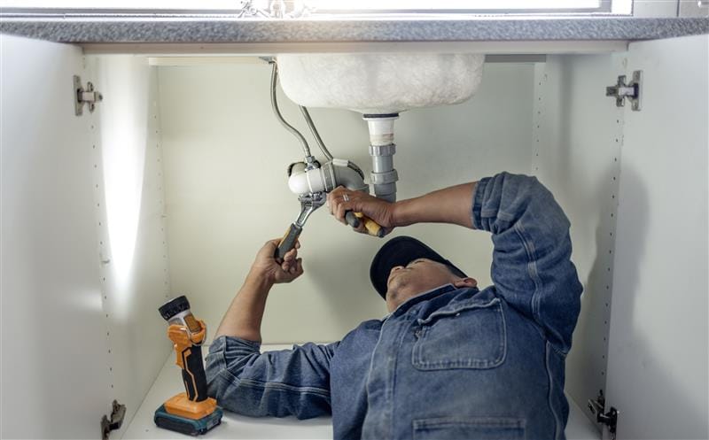 Plumber repairing pipes beneath a bathroom sink in Prescott