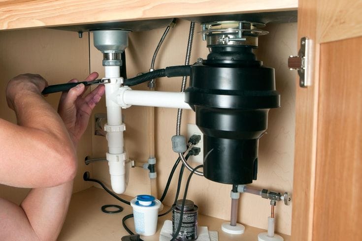 Plumber installing a garbage disposal beneath a kitchen sink in Prescott