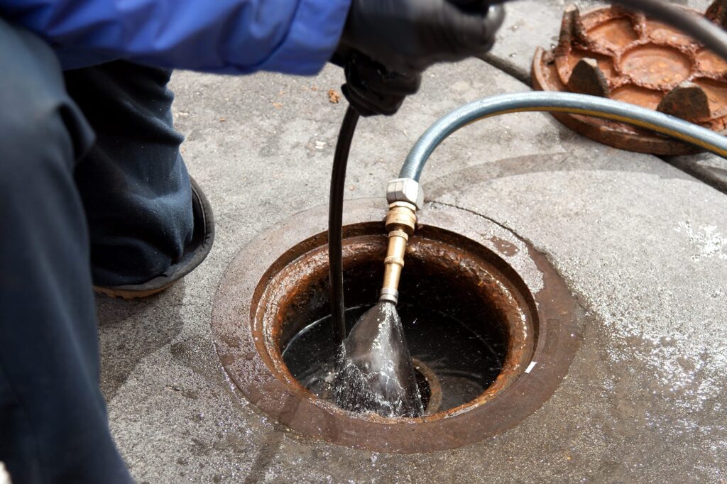 Plumber hydro jetting a sewer line through a manhole in Prescott