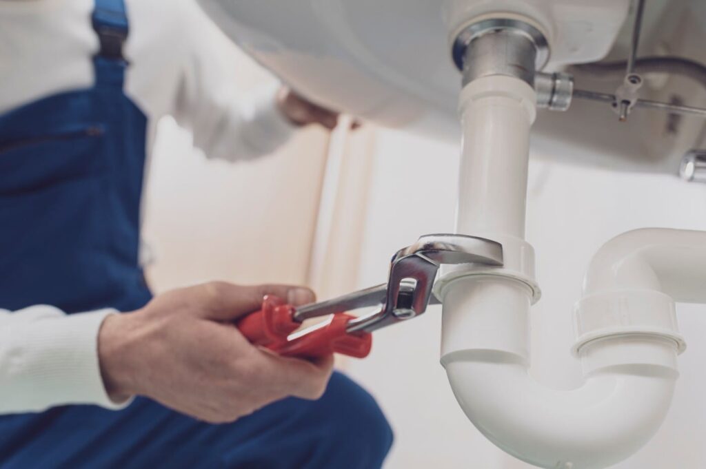 Plumber repairing a white drain pipe beneath a sink in Prescott