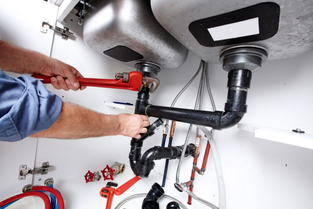 Plumber repairing drain pipes beneath a kitchen sink in Prescott